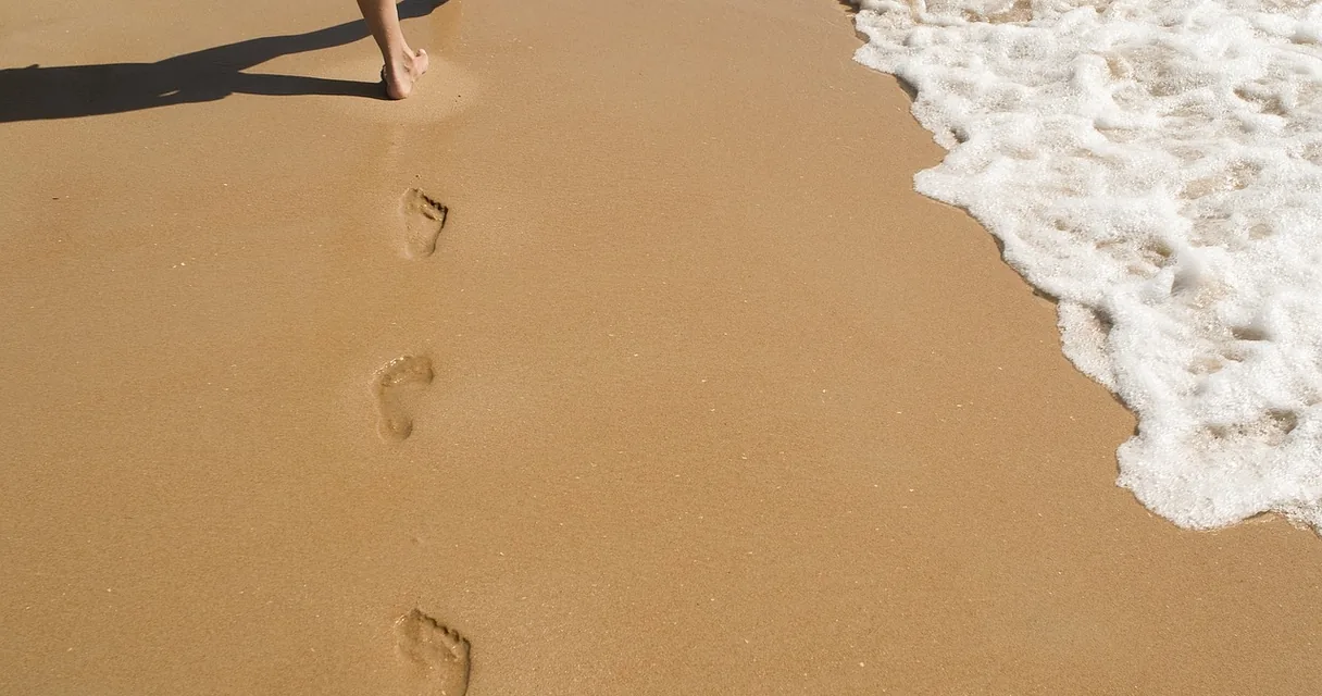 Pegadas de pés descalços na areia da praia, ilustrando a ardência na lateral da coxa