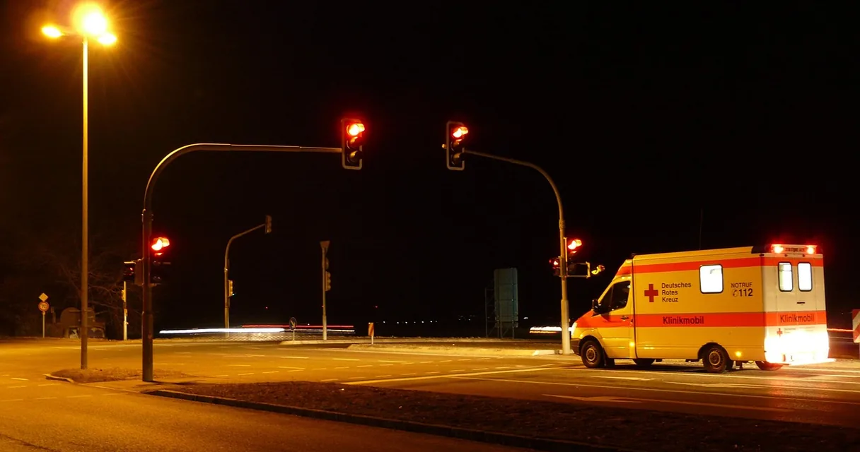 Ambulância com luzes acesas parada em um cruzamento à noite, ilustrando a queda com dor forte na virilha
