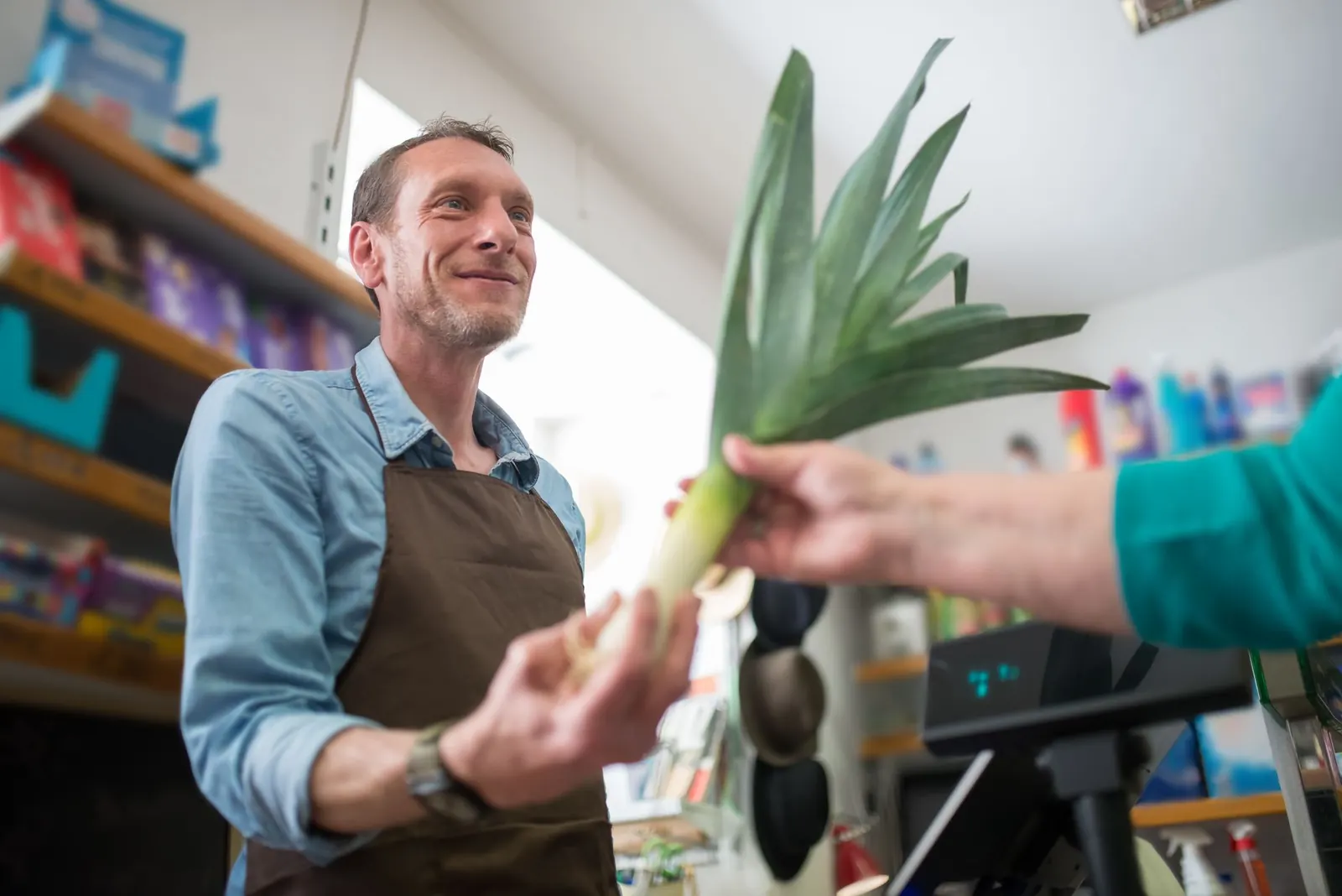 Lojista entregando verduras a uma cliente no balcão de uma mercearia