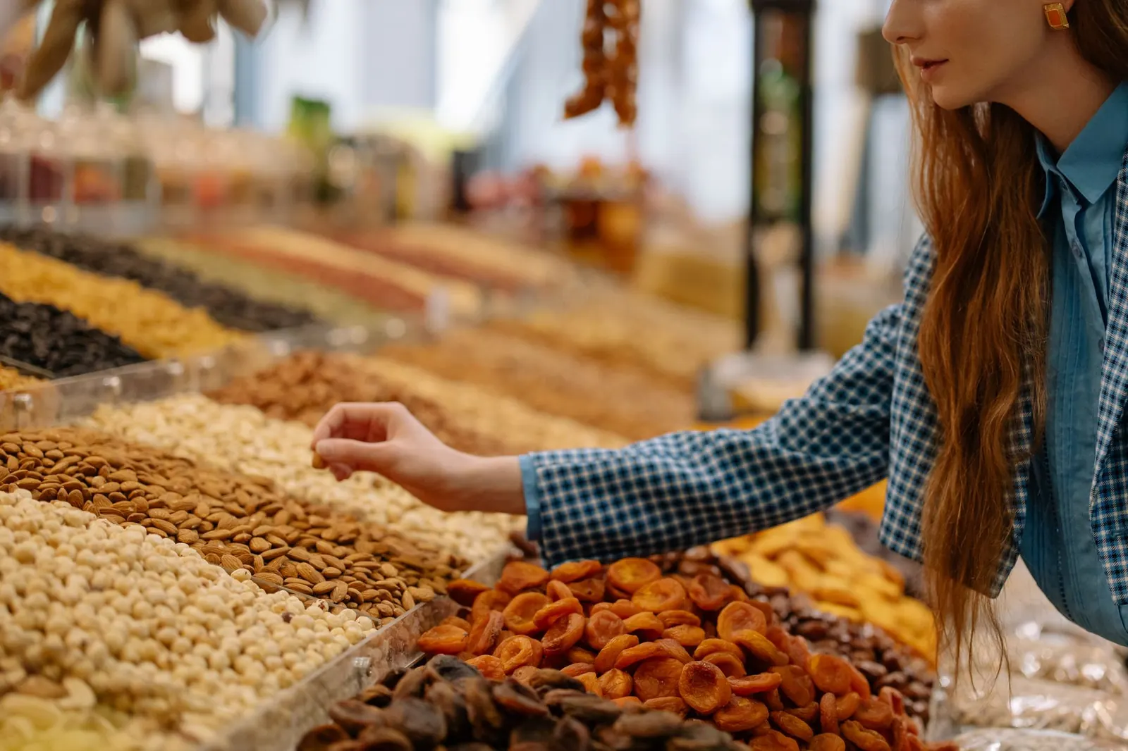 Mão escolhendo damascos secos numa banca de castanhas e frutas secas a granel
